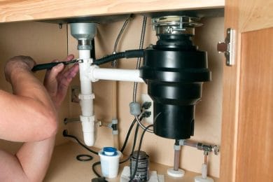 Plumber repairing a garbage disposal beneath a kitchen sink in Murrysville